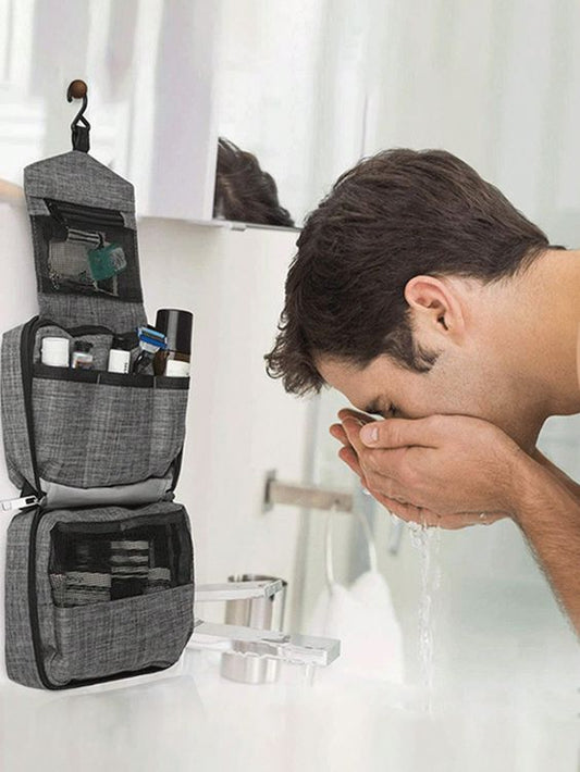 grey-hanging toiletry bag- bathroom- man- sink- washing face- skincare- front to side angle- unfolded bag